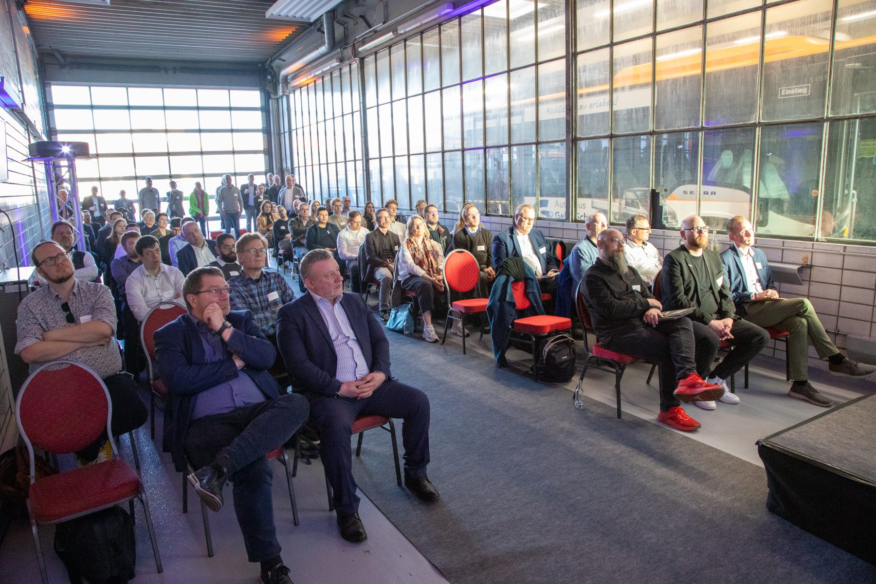 Gäste des SpringEvents sitzen in Reihen in Werkshalle und hören Vorträgen zu